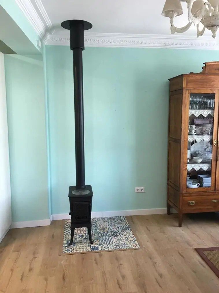 Jøtul F 602 ECO negra instalada por Chimeneas Ferrol en un salón, con tubo vertical hasta el techo y protector de suelo de baldosa hidráulica